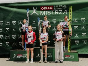 Powiększ obraz: Grupa dzieci i młodzieży na podium zwycięzców zawodów skoków narciarskich, z medalami i pucharami